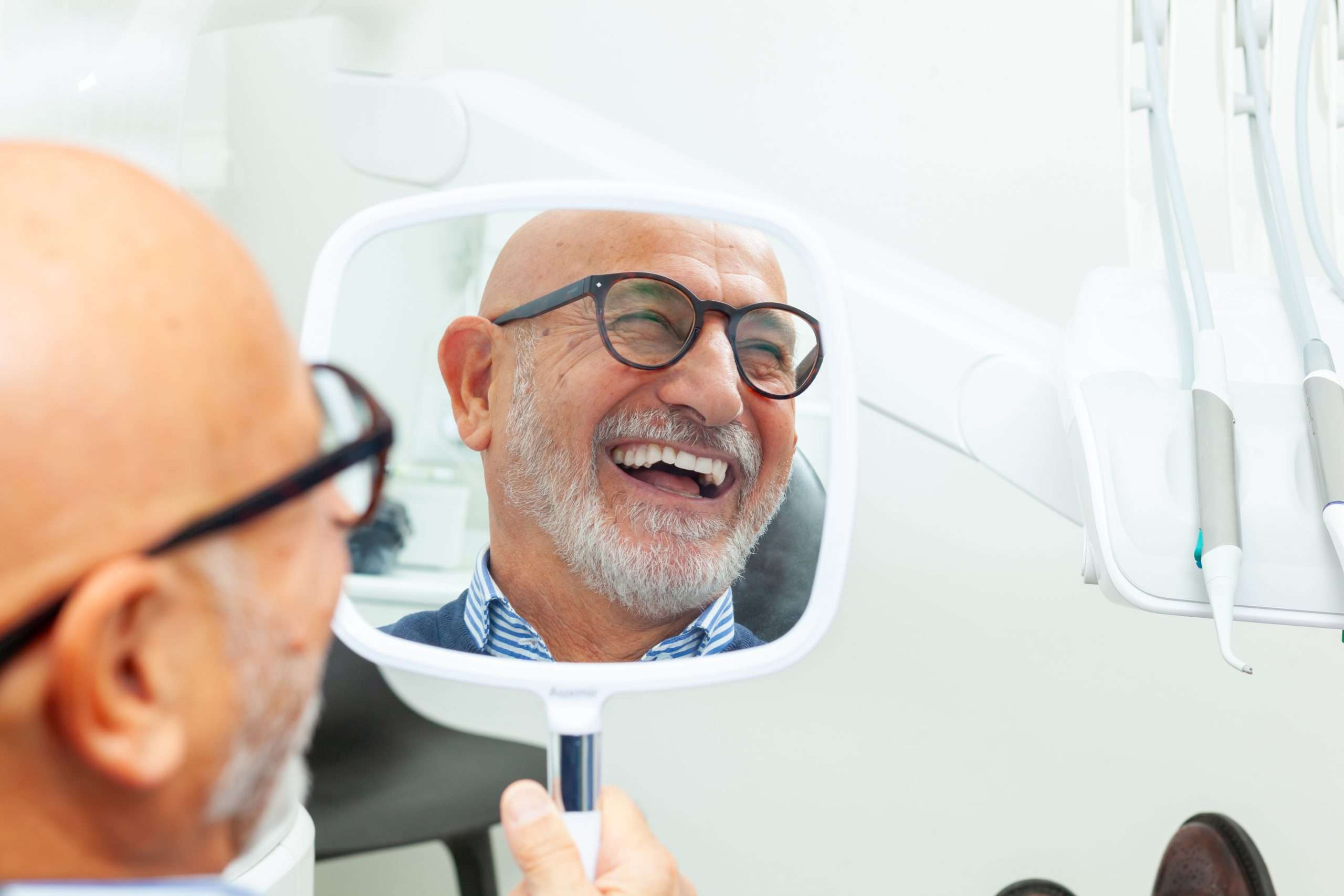 a happy customer looking in the mirror at his new all-on-4 dental implants that he got at abington dental in clarks summit, pa